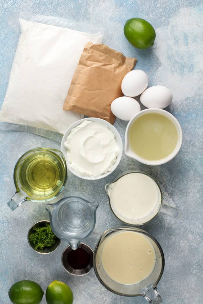 Ingredients for key lime poke cake arranged on a blue countertop.