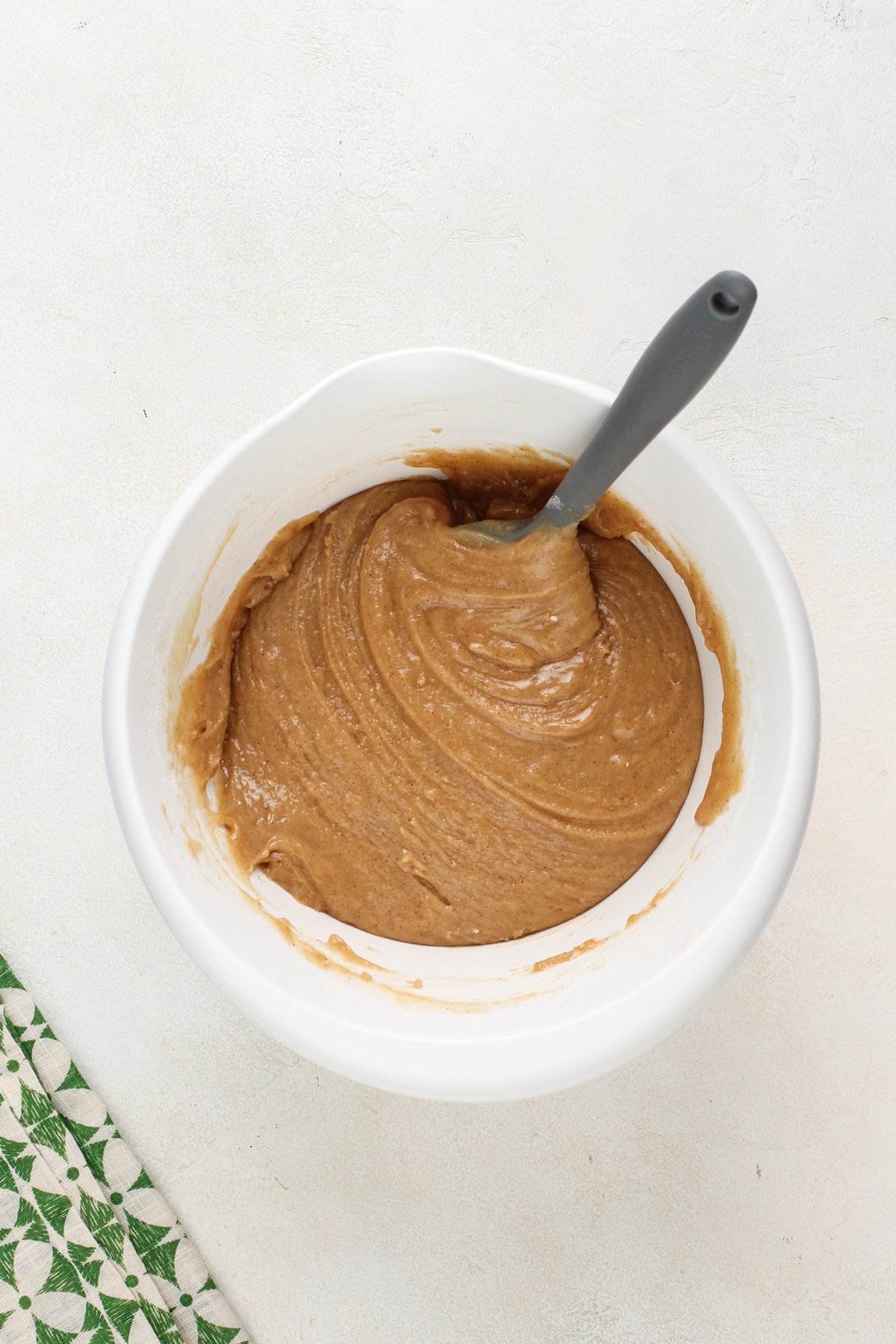 Batter base for zucchini muffins being stirred with a spatula in a white bowl.