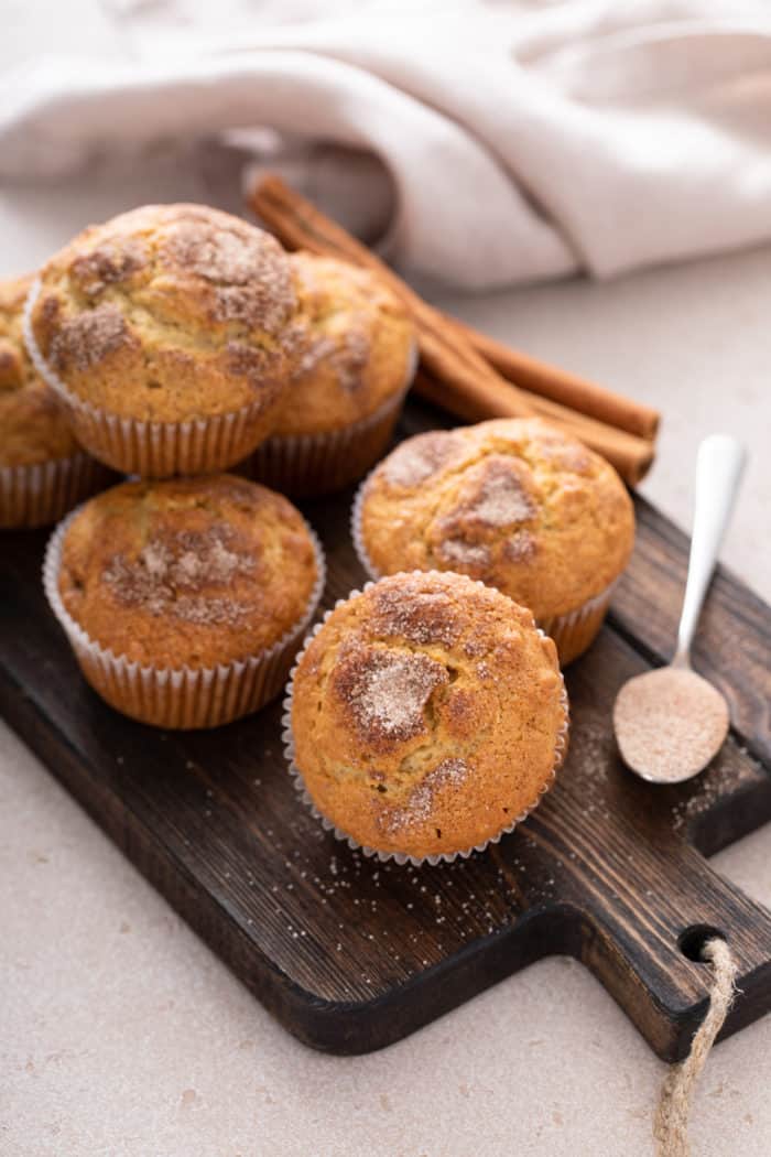 Muffins topped with cinnamon sugar set on a wooden board.