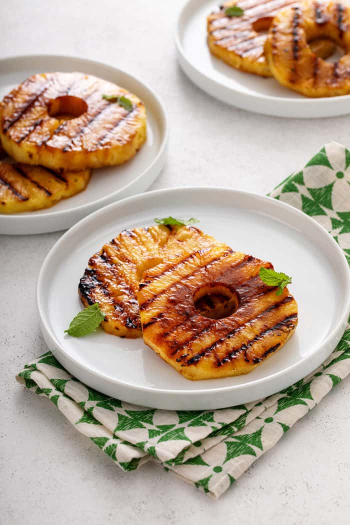 Three white plates, each with two slices of grilled pineapple.