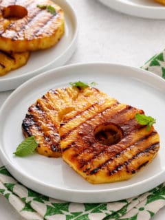 Plated slices of grilled pineapple garnished with mint leaves.