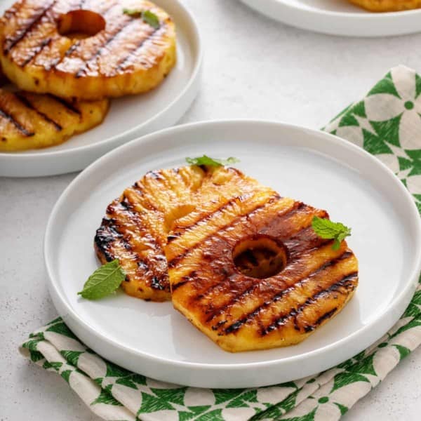 Plated slices of grilled pineapple garnished with mint leaves.