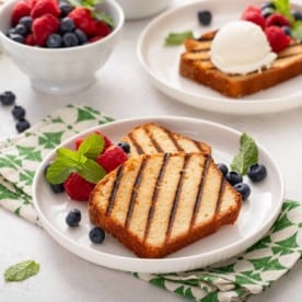 Two white plates, each holding grilled pound cake and fresh berries.