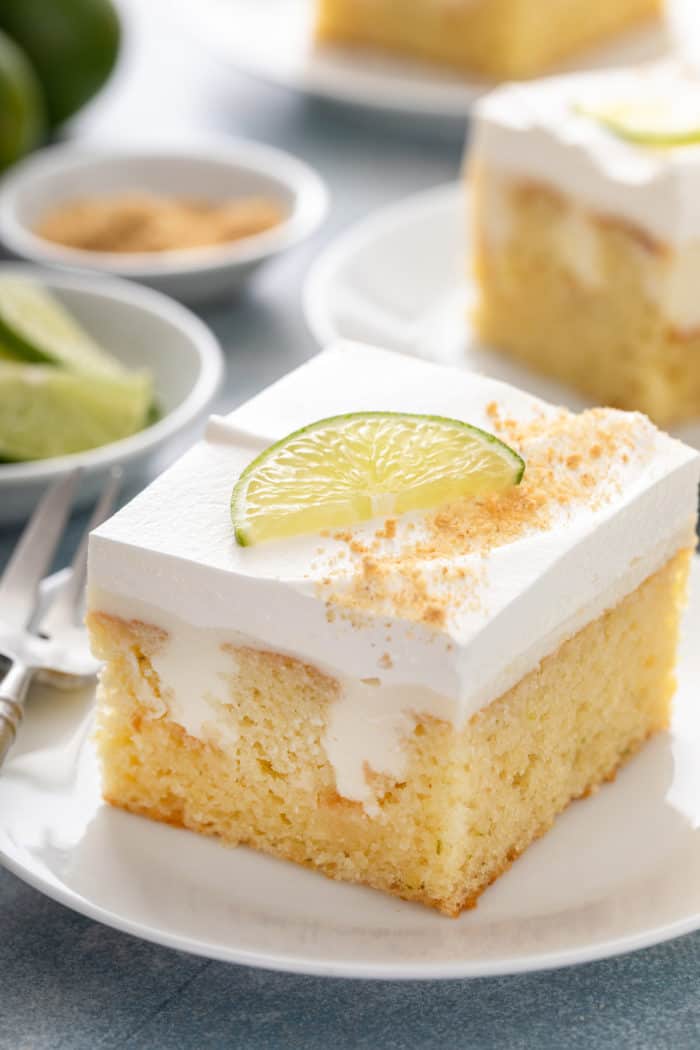 Slice of key lime poke cake garnished with a lime slice on a white plate.