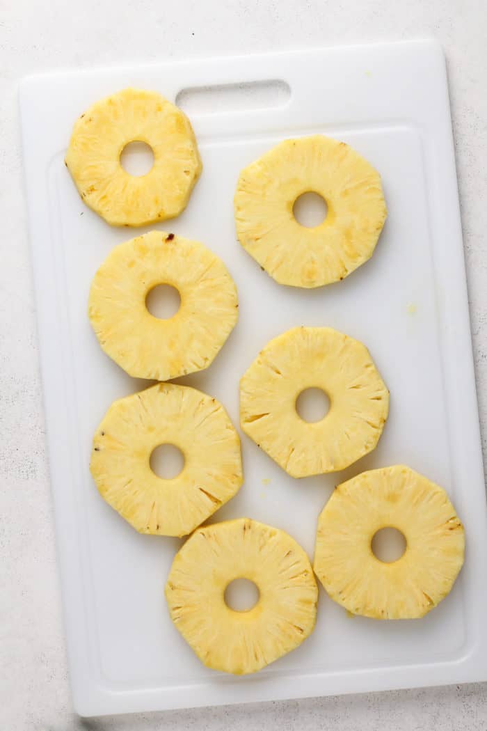 Slices of pineapple on a white cutting board with the cores removed.