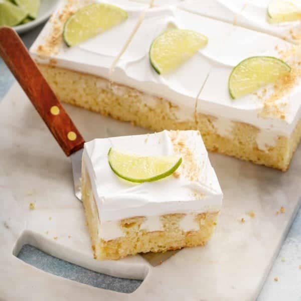 Cake server holding a slice of key lime poke cake with more slices of the cake in the background.