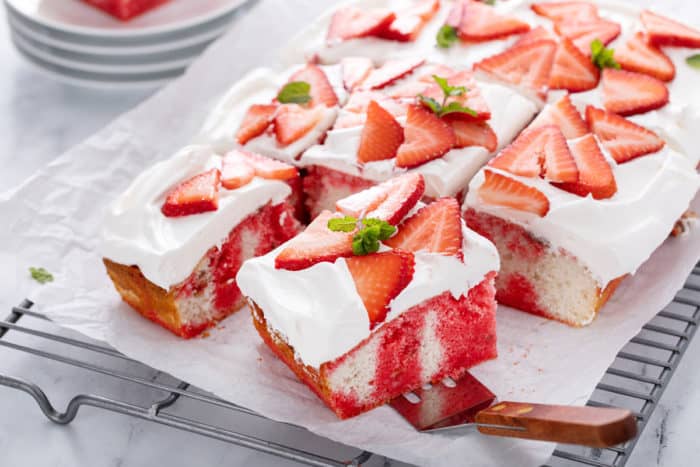 Cake server about to lift a slice of strawberry poke cake up from the rest of the cake.