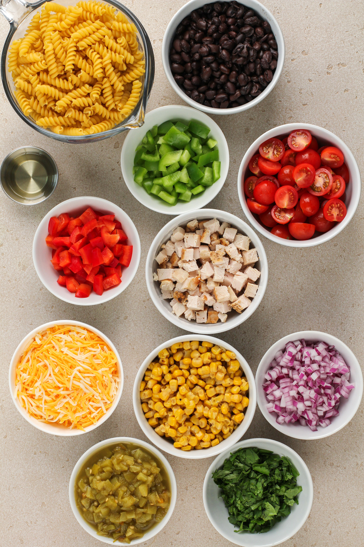 Pasta and mix-ins for southwest pasta salad arranged on a beige countertop.