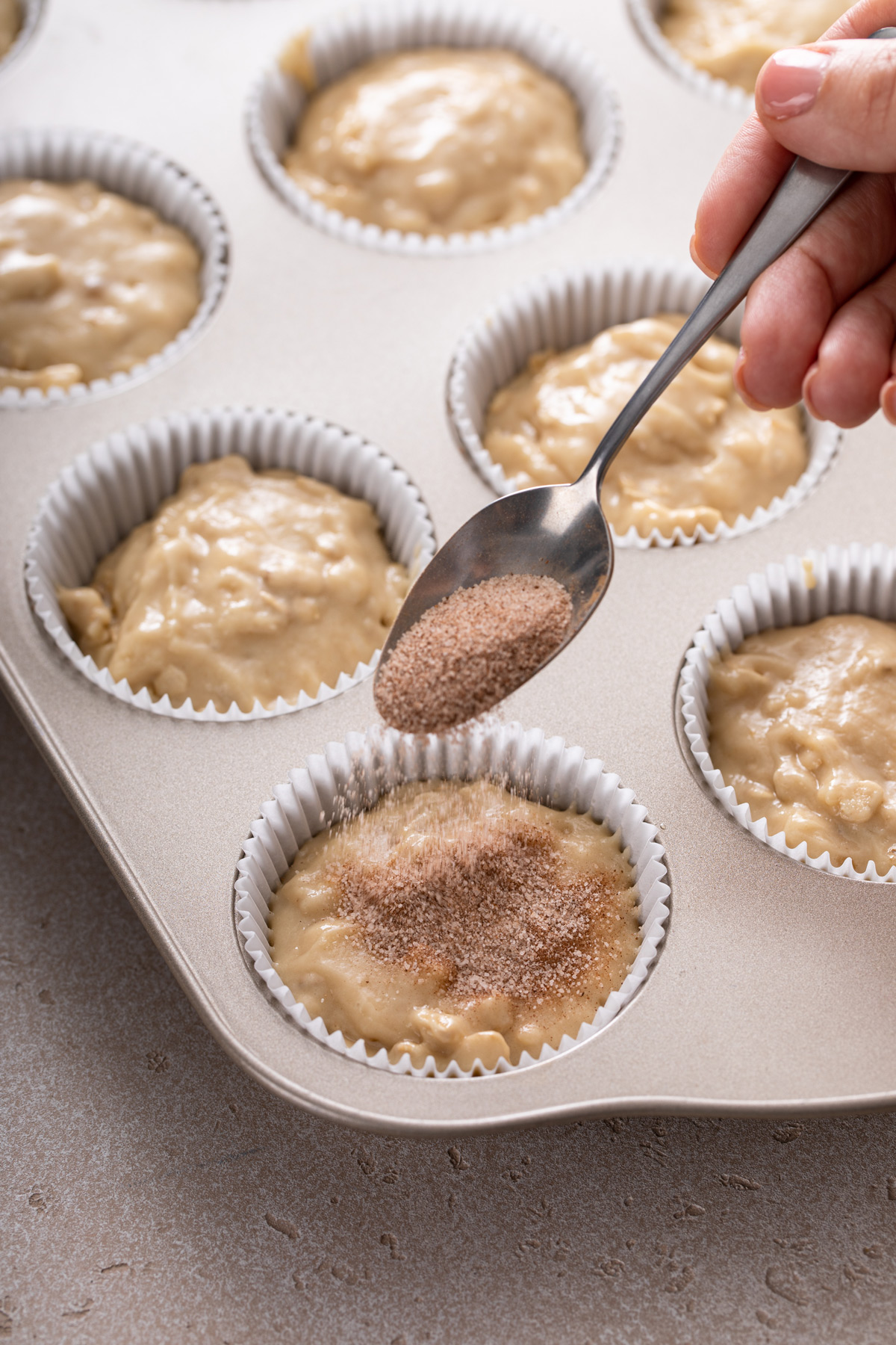 Cinnamon sugar being spooned over muffin batter before baking.