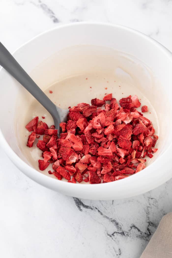 Crushed freeze-dried strawberries being folded into white cake batter in a white mixing bowl.