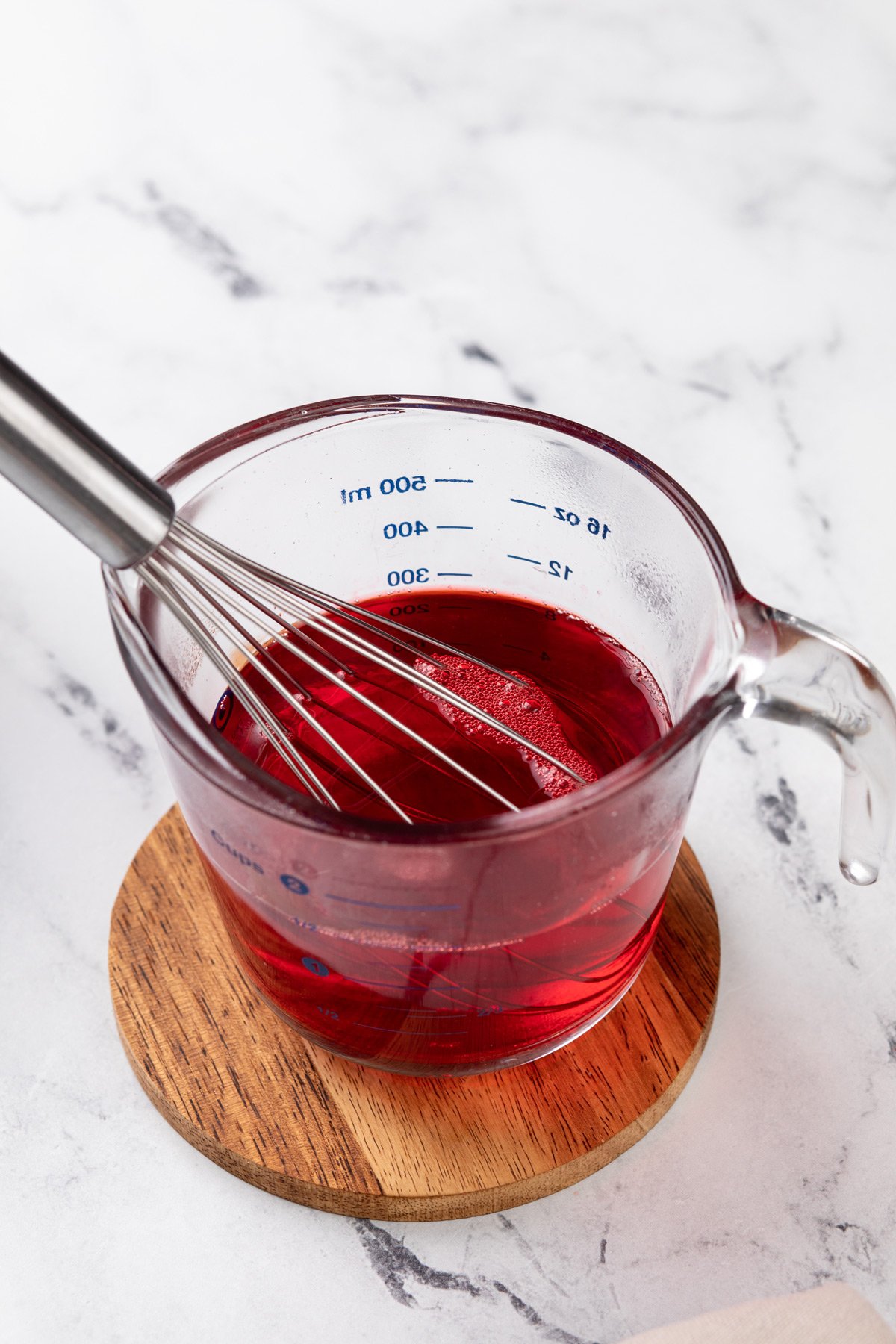 Strawberry jello mixture being whisked in a glass measuring cup.