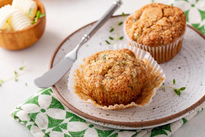 Two zucchini muffins on a plate. One of them is unwrapped from the paper wrapper.