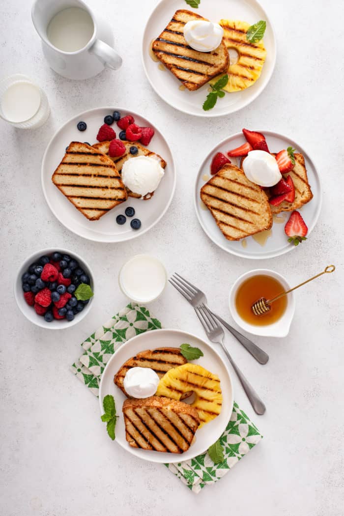 Four white plates, each holding a serving of grilled pound cake with a different kind of fruit.