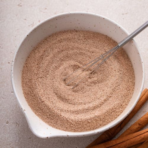 Cinnamon sugar and a small whisk in a white bowl.