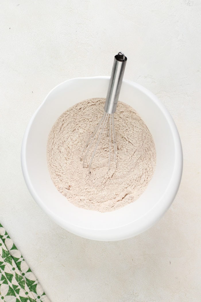 Dry ingredients for zucchini muffins being whisked in a white mixing bowl.