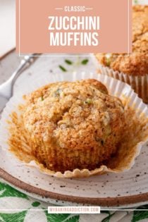 Two zucchini muffins on a plate. One of them is unwrapped from the paper wrapper. Text overlay includes recipe name.