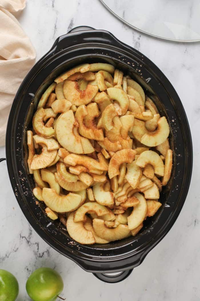 Sliced apples tossed with spices in the crock of a slow cooker.