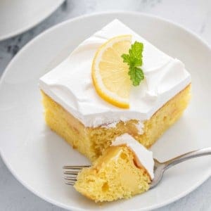 Fork taking a bite from a slice of lemon poke cake.