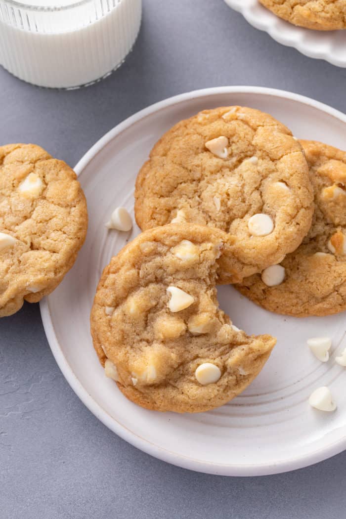 Several white chocolate macadamia nut cookies on a white plate. One cookie has a bite taken out of it.