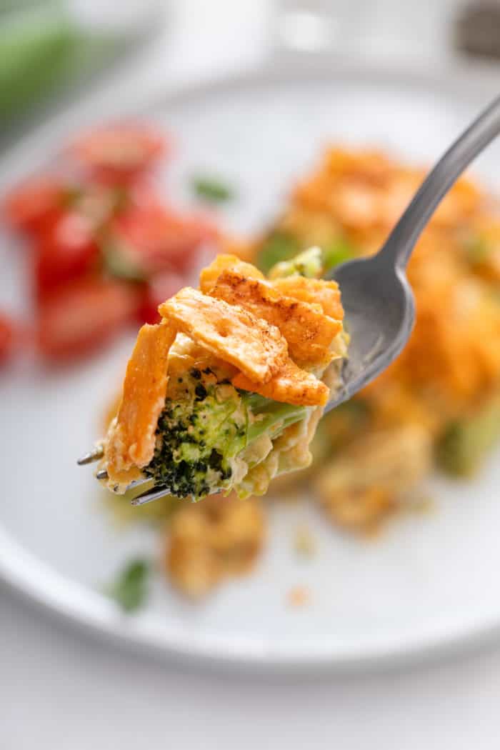 Fork holding a bite of broccoli casserole up to the camera.