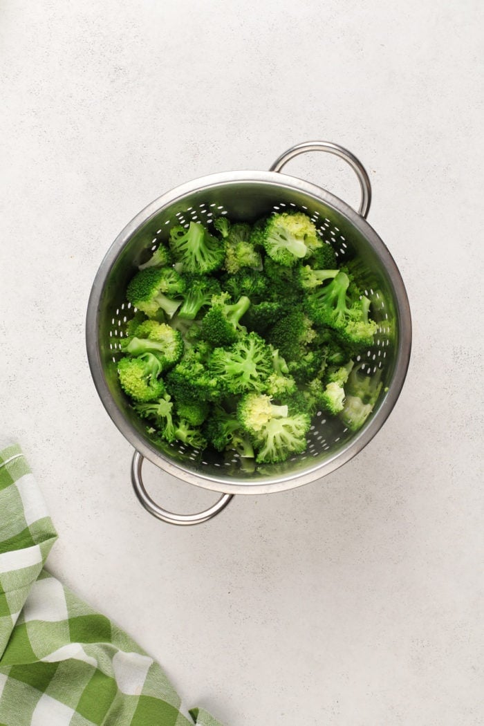 Blanched broccoli florets in a metal colander.