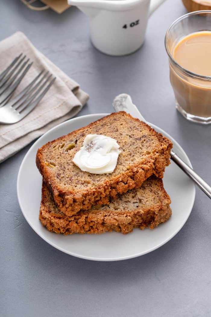 Two slices of brown butter banana bread stacked on a white plate, with a smear of butter on the top slice.