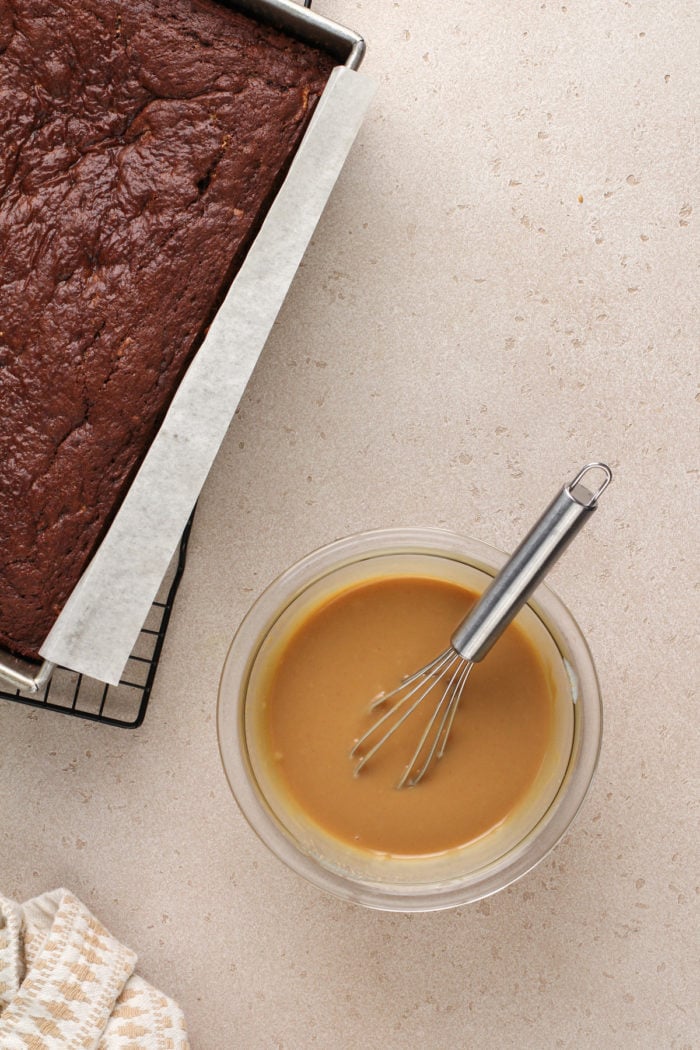 Peanut butter filling for butterfinger poke cake in a glass bowl next to a chocolate butterfinger cake.