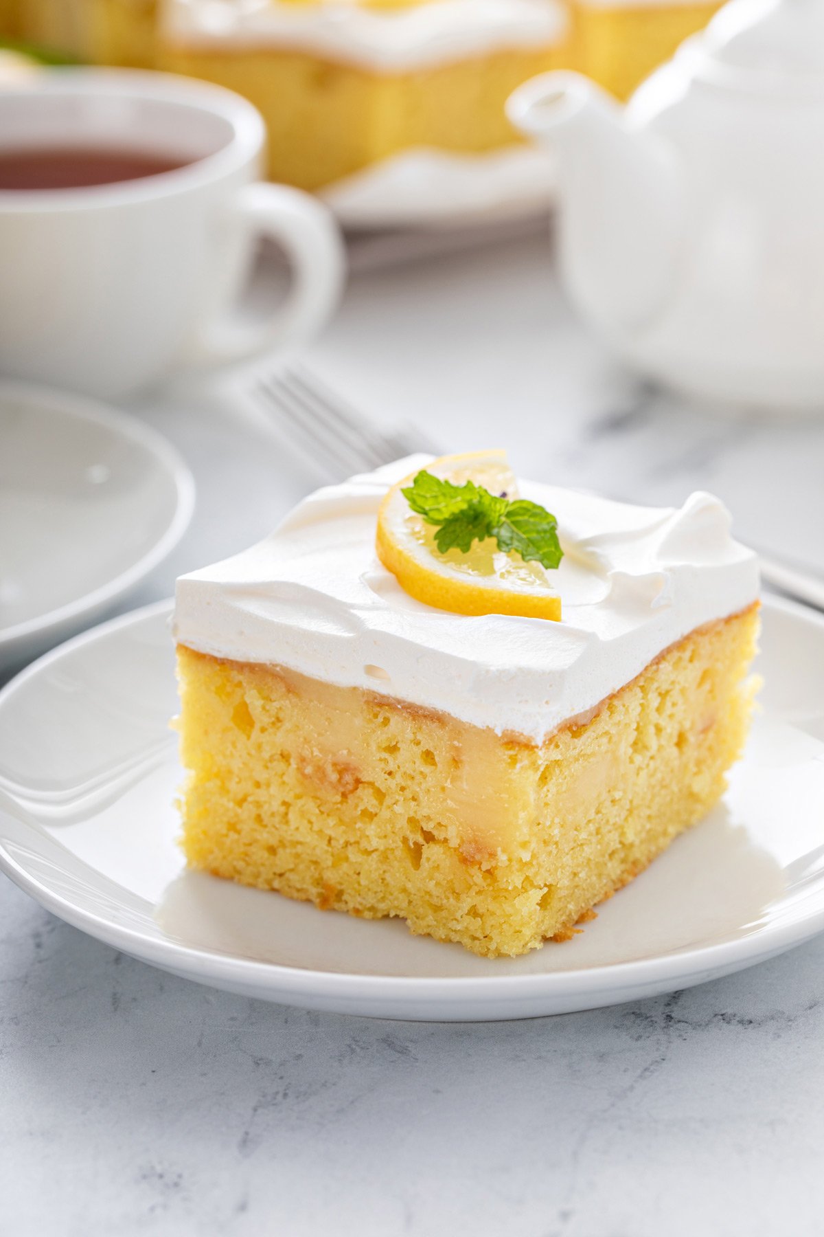 Close up image of a slice of lemon poke cake on a white plate.