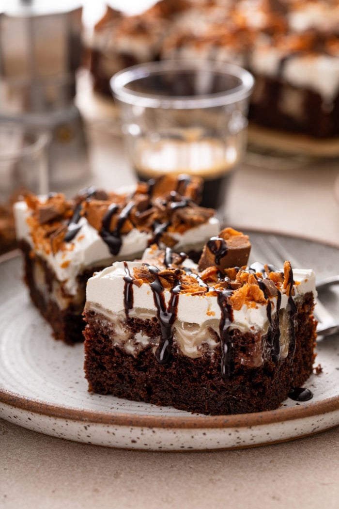 Side view of two slices of butterfinger poke cake on a stoneware plate.