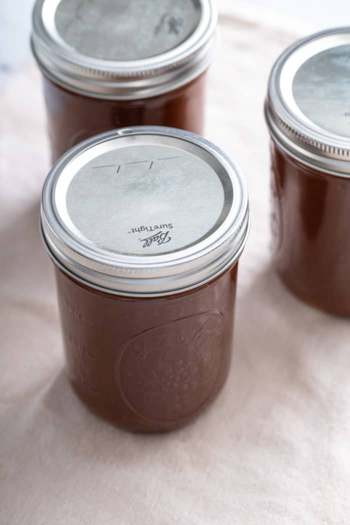 Jars of apple butter cooling on a kitchen towel.