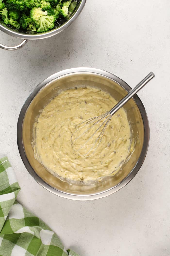 Cream base for broccoli casserole being whisked in a metal mixing bowl.