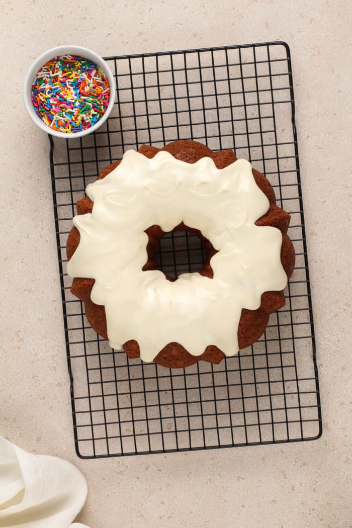 Cream cheese frosting spread over a vanilla bundt cake set on a wire rack.