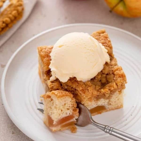Fork cutting a bite from the corner of a slice of easy apple coffee cake topped with vanilla ice cream.