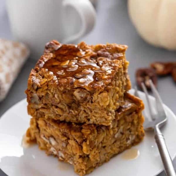 Two slices of pumpkin baked oatmeal stacked on a white plate and drizzled with maple syrup.