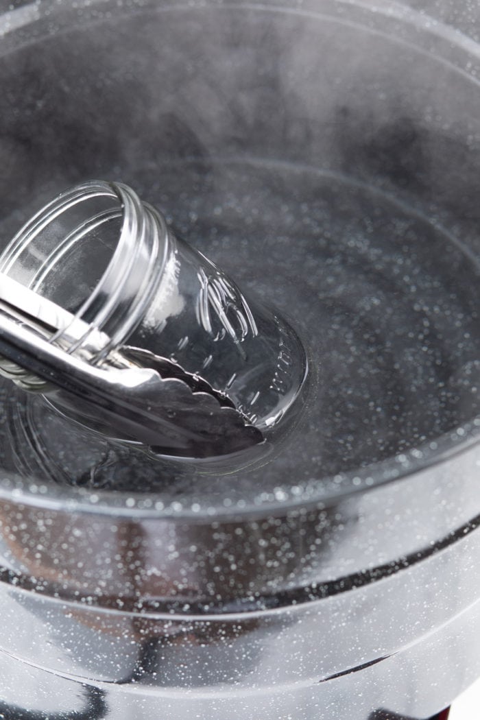 Jar being dunked in a canning water bath to warm it through.