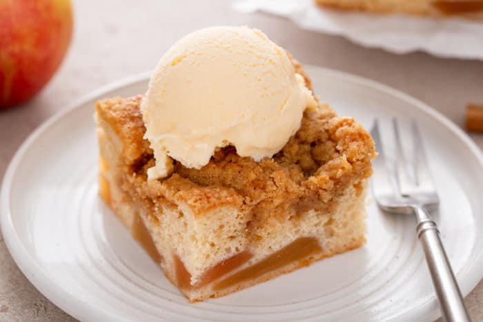 Slice of easy apple coffee cake topped with a scoop of vanilla ice cream on a white plate.
