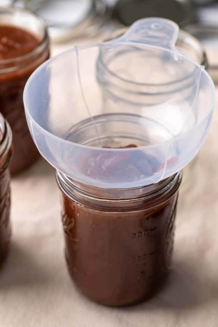 Apple butter being added to jars with a canning funnel.