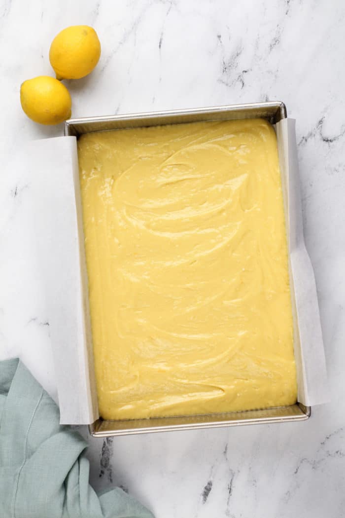 Lemon cake batter spread into a 13x9-inch pan lined with parchment paper.