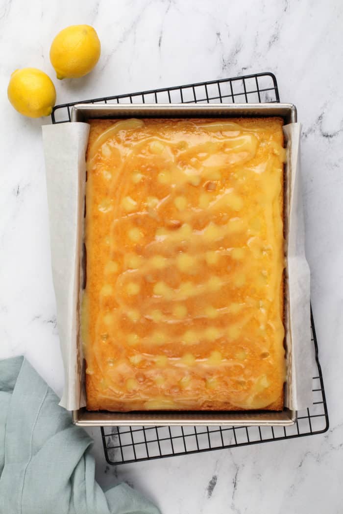 Lemon curd spread over a lemon cake with holes poked across the top.