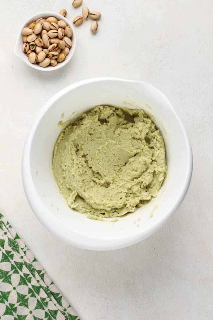 Cookie dough base for white chocolate pistachio pudding cookies mixed in a white mixing bowl, ready to have white chocolate chips and chopped pistachios added to it.