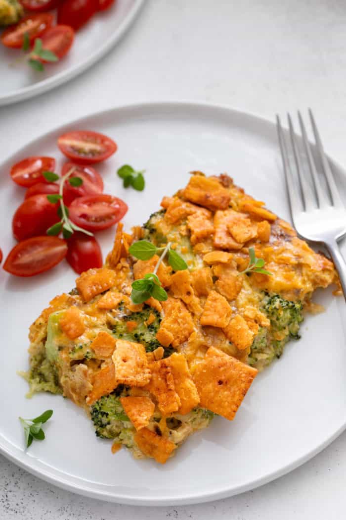 Broccoli casserole next to a fork and a tomato salad on a white plate.