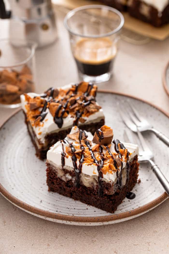 Two slices of butterfinger poke cake next to two forks on a stoneware plate.