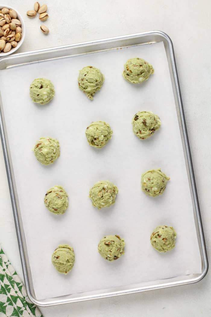 Dough balls for white chocolate pistachio pudding cookies lined up on a parchment-lined baking sheet.