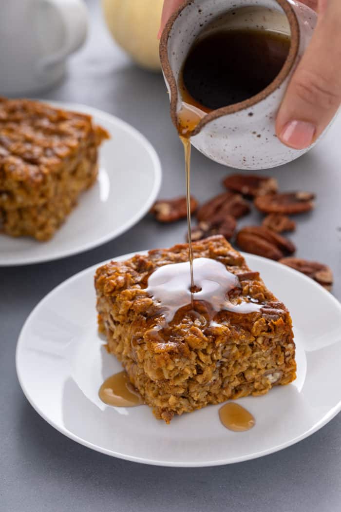 Maple syrup being drizzled on top of a slice of pumpkin baked oatmeal on a white plate.