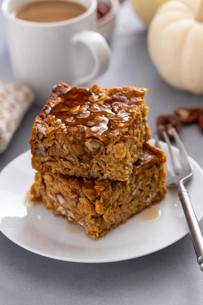 Two slices of pumpkin baked oatmeal stacked on a white plate and drizzled with maple syrup.