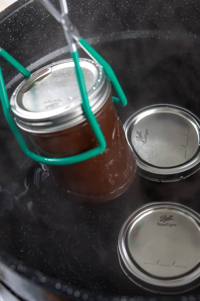 Jar lifter taking a jar of canned apple butter out of the water bath.