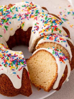 Sliced vanilla bundt cake topped with cream cheese frosting and sprinkles.