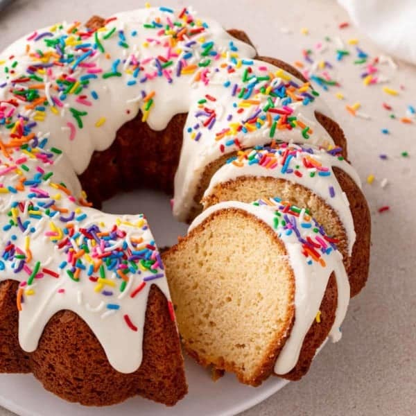 Sliced vanilla bundt cake topped with cream cheese frosting and sprinkles.