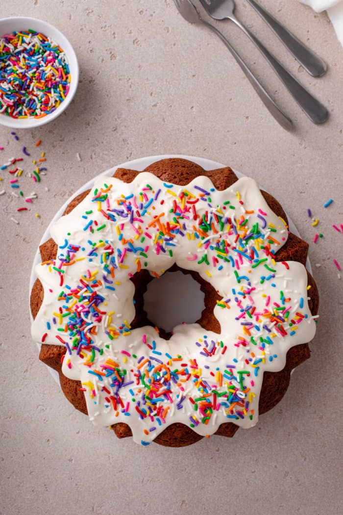Overhead view of a vanilla bundt cake topped with cream cheese frosting and rainbow sprinkles.