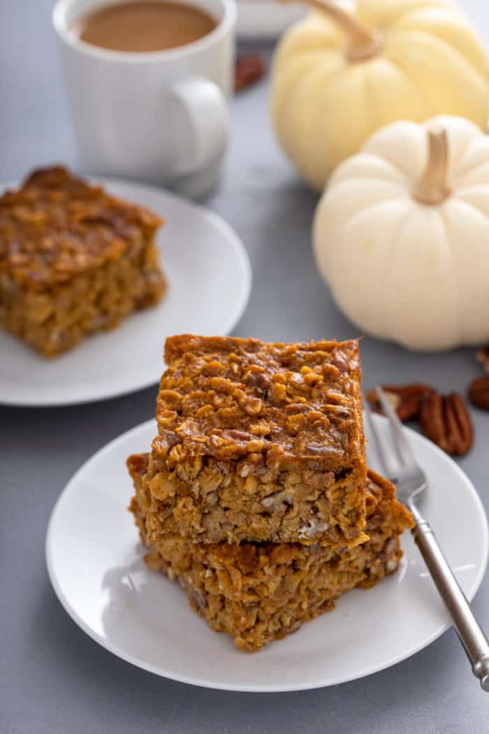 Two slices of pumpkin baked oatmeal stacked on a white plate next to a fork.
